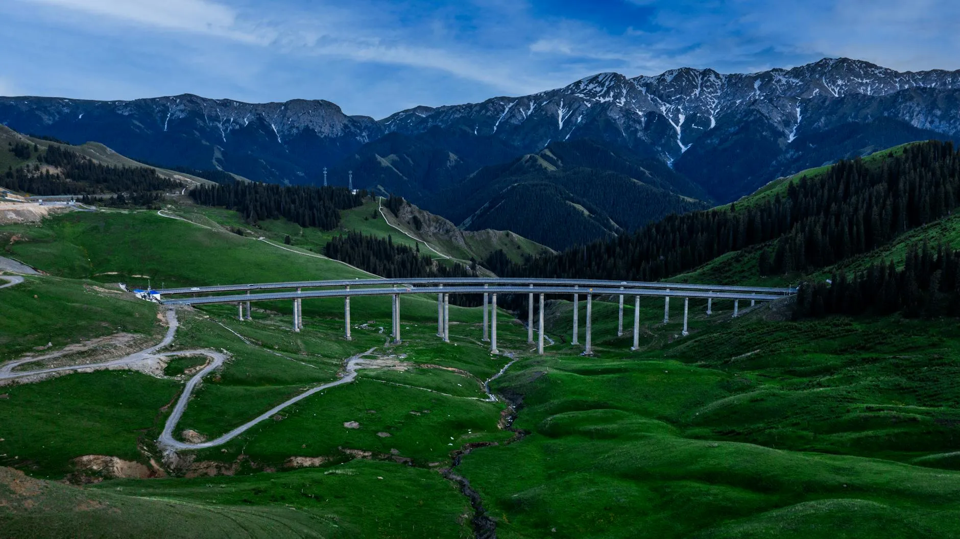 Ili Valley, Xinjiang — Aerial photo of a bridge spanning a lush green valley in Ili, Xinjiang, China, with mountain backdrop.