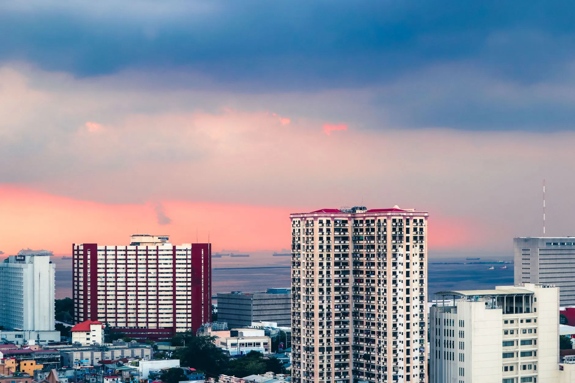 Manila, Philippines — high-rise towers above Manila Bay at sunset, with cargo ships anchored offshore