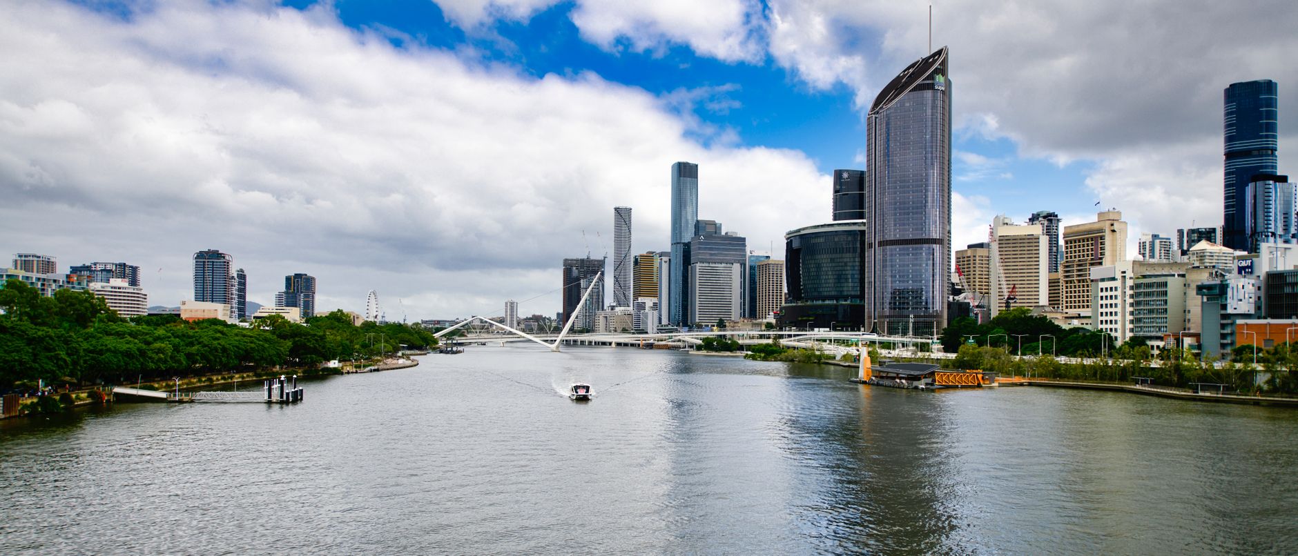 The Brisbane River and city skyline on a bright day, with a CityCat ferry and the Kurilpa Bridge