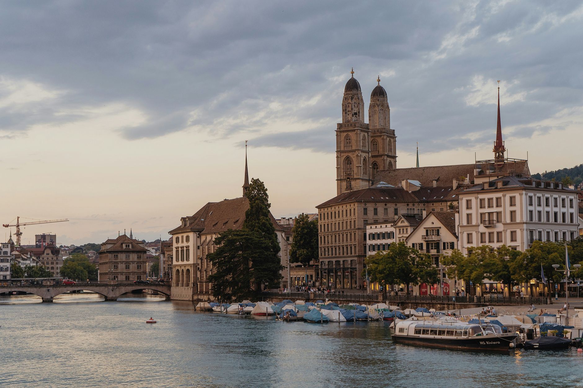Scenic Zurich cityscape featuring the Grossmünster church along the Limmat River at dusk.