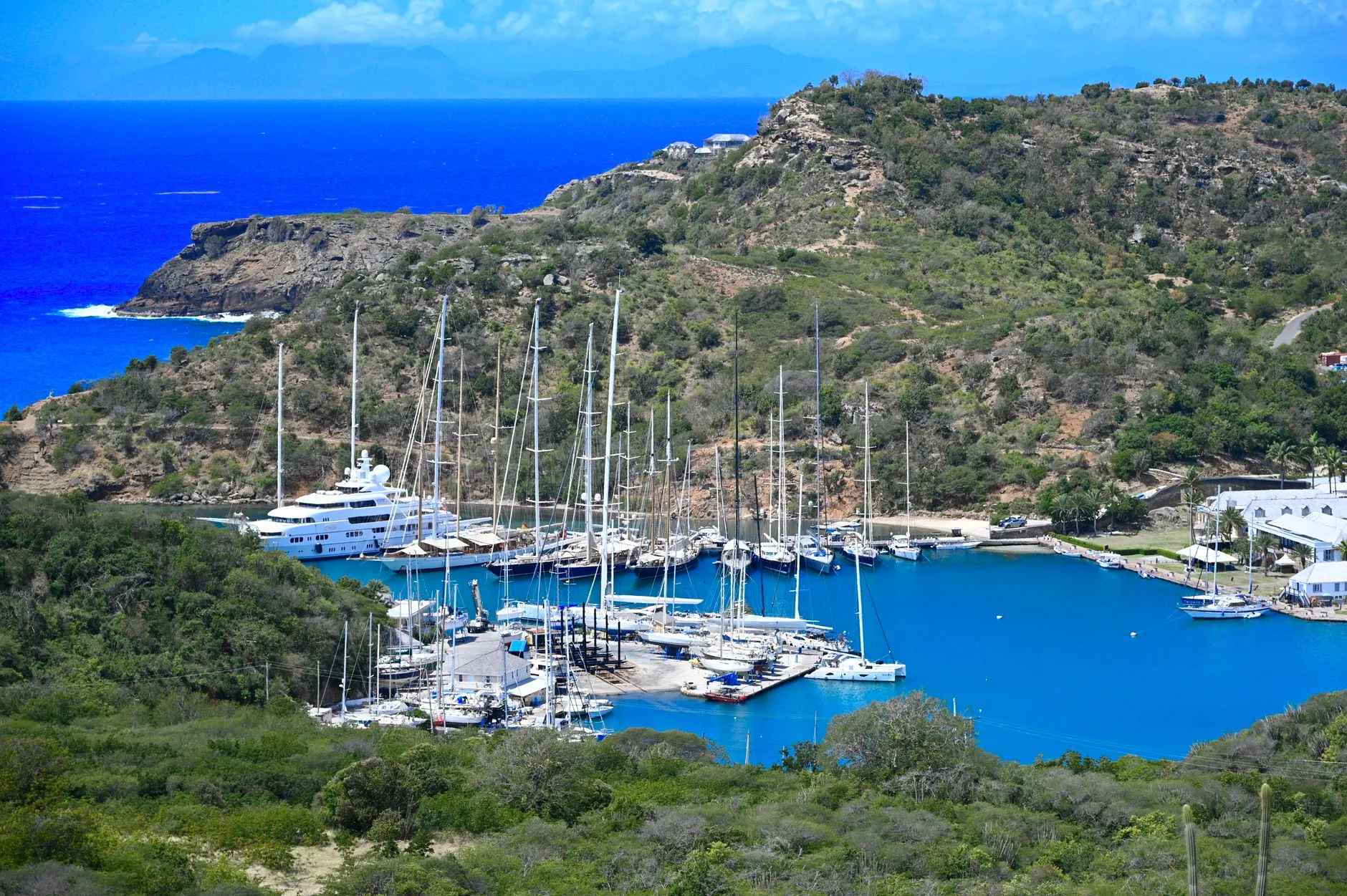 Sailing yachts and superyachts moored in a sheltered natural harbour ringed by green hills, Antigua