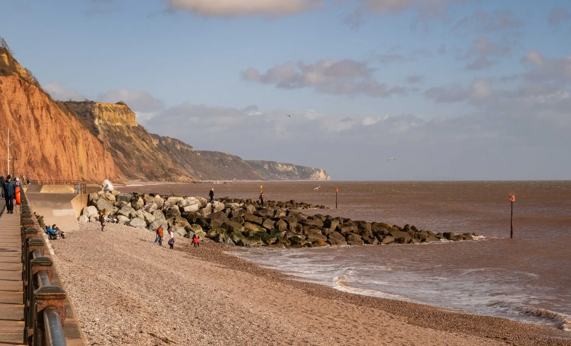 Exeter, Devon — Pebble beach with people enjoying the views of red cliffs and sea at Sidmouth, Devon, England.