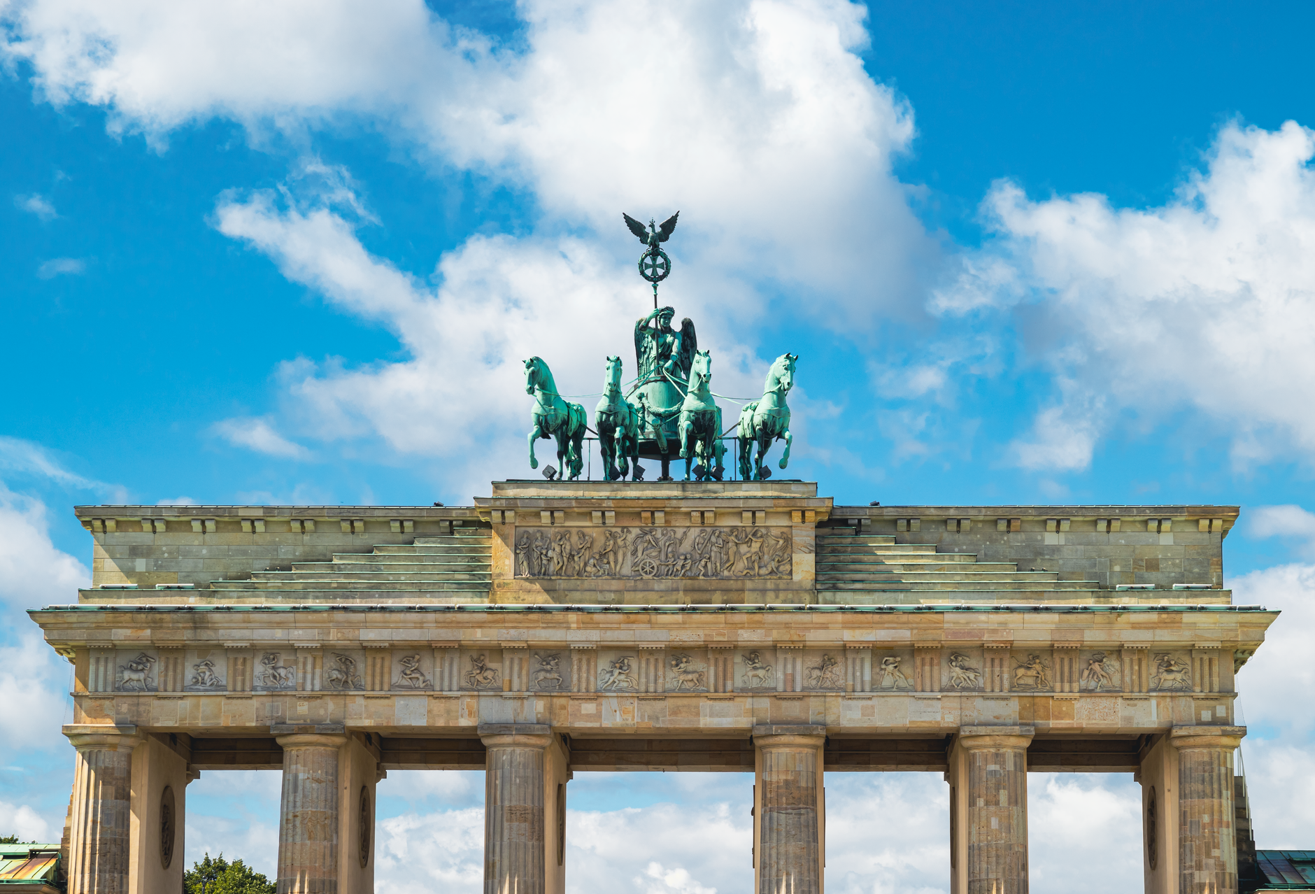 The iconic Brandenburg Gate in Berlin, Germany, beneath a vibrant blue sky with clouds.