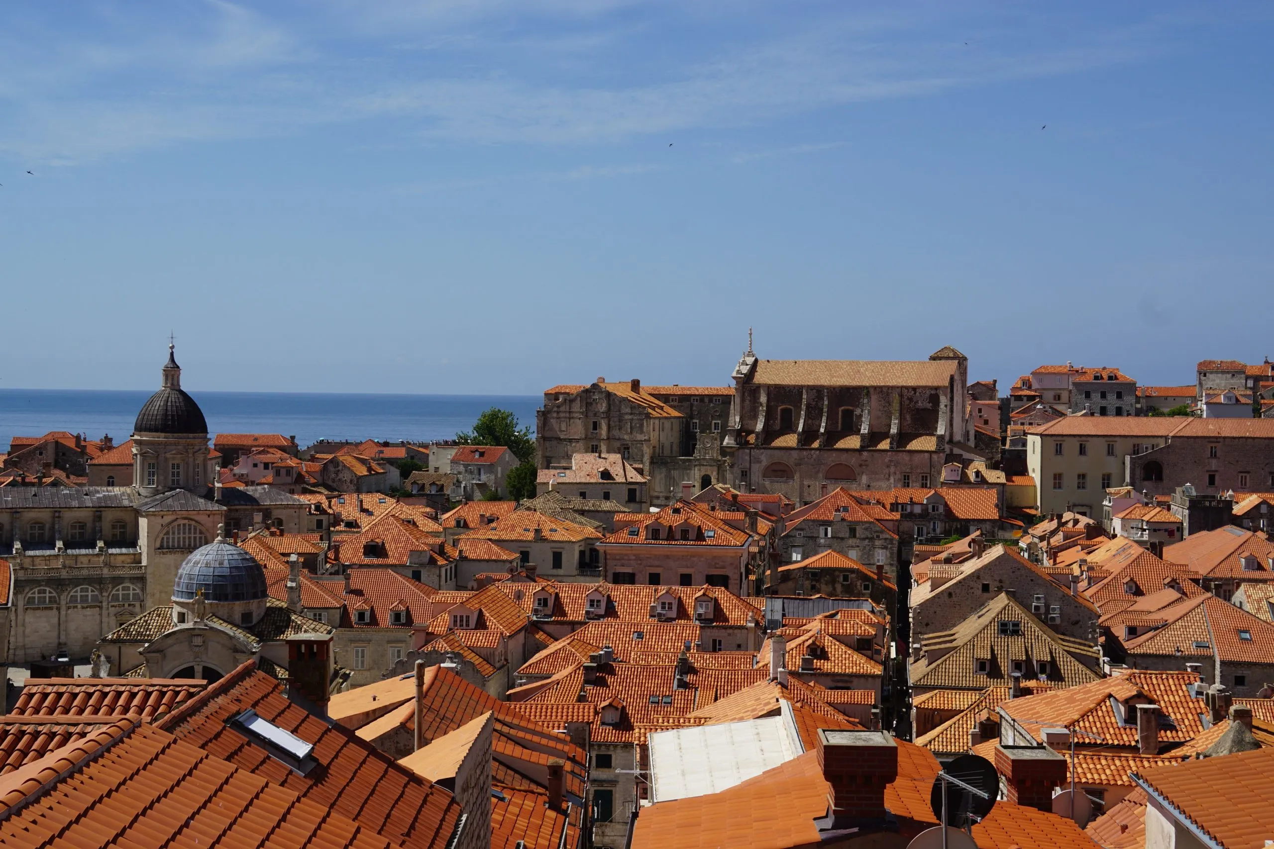 Aerial view of Dubrovnik's historic red rooftops against a clear blue sky and the Adriatic Sea.