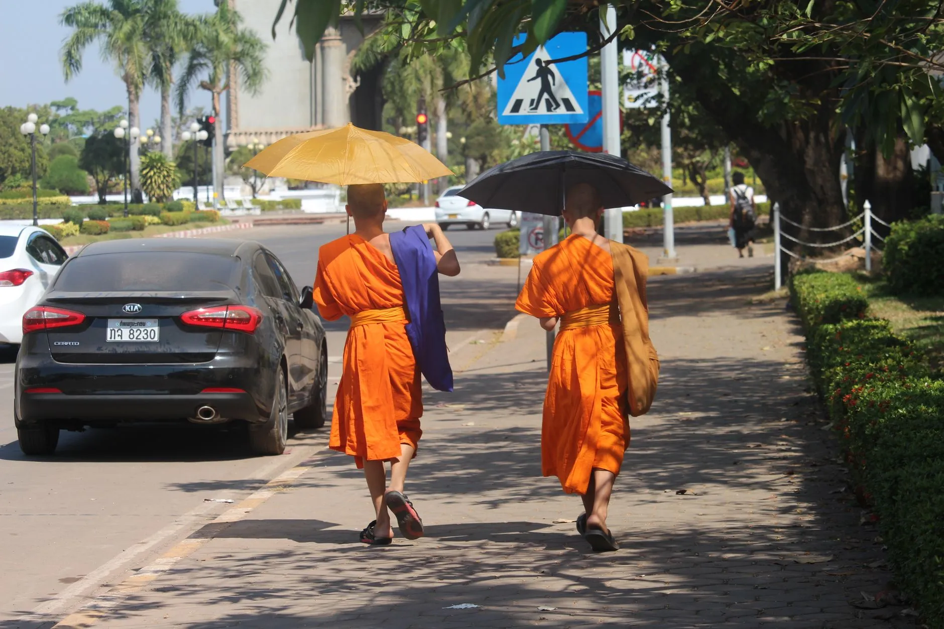 Two Buddhist monks walking on a sunny sidewalk in Vientiane, Laos with umbrellas for shade.
