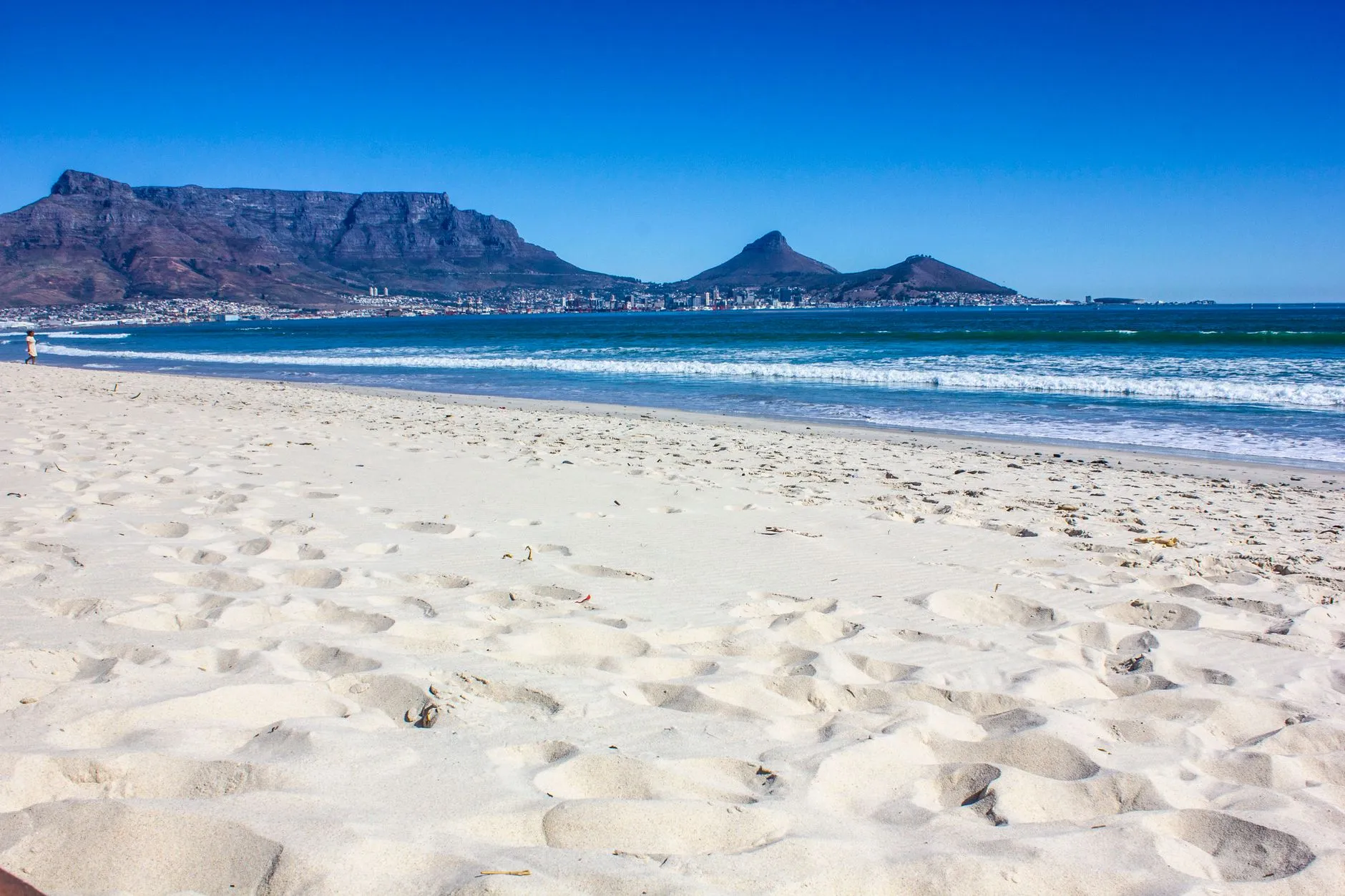 Cape Town — Table Mountain, Devil's Peak and Lion's Head seen across Table Bay from a white-sand beach under a clear blue sky, South Africa