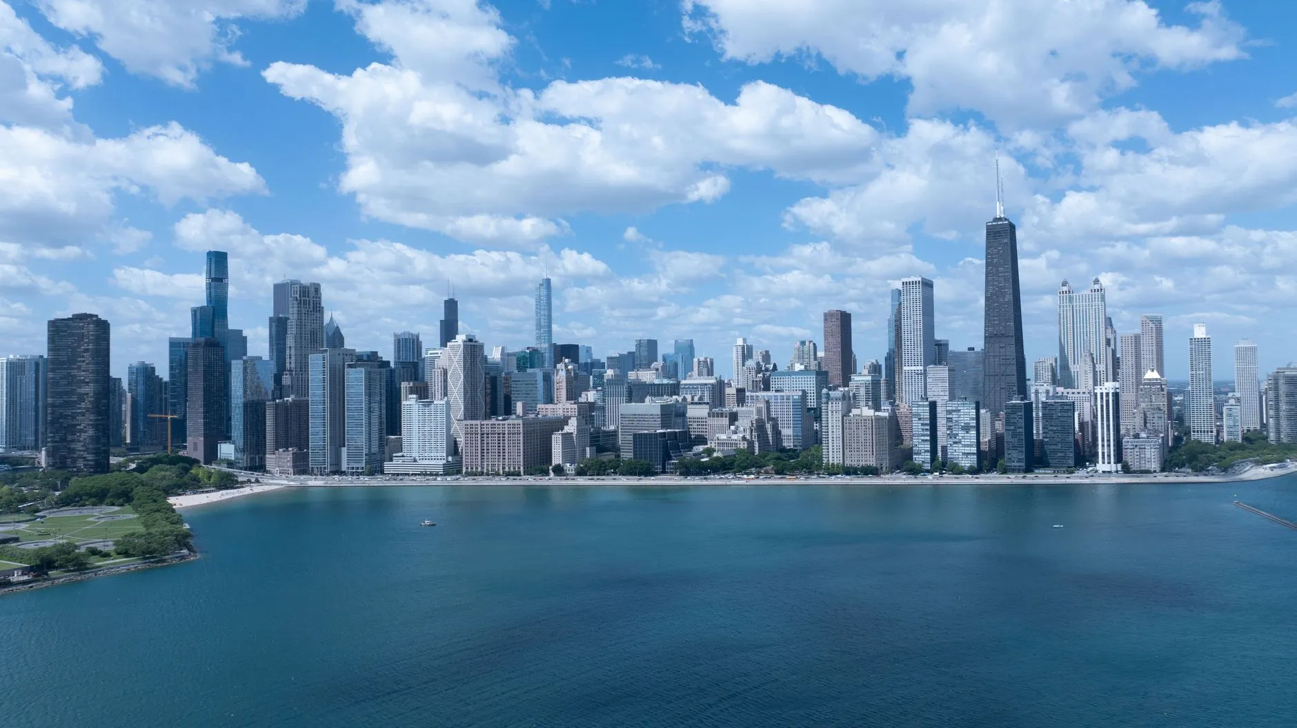 Chicago — the downtown skyline seen across Lake Michigan under a bright blue sky, with the John Hancock Center and the lakefront beach