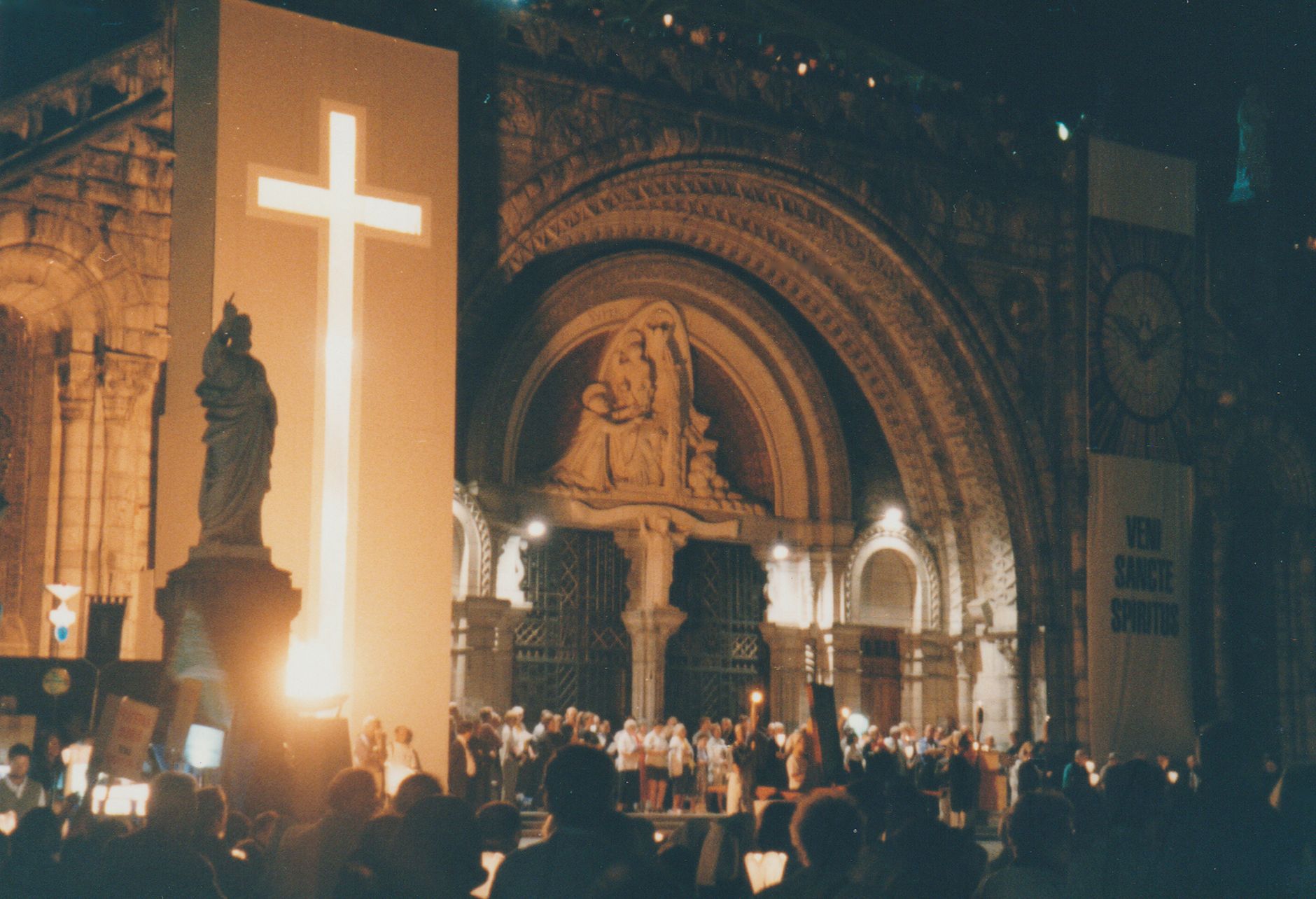 Lourdes and the Pyrenees, France — Night view of a lit cross and crowd at Lourdes Basilica, France.