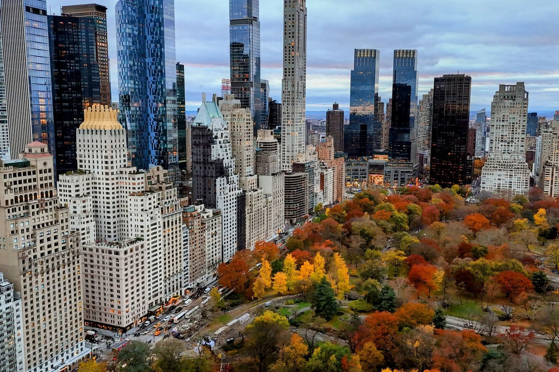 an aerial view of central park surrounded by new york city's skyscrapers in vibrant fall colors.