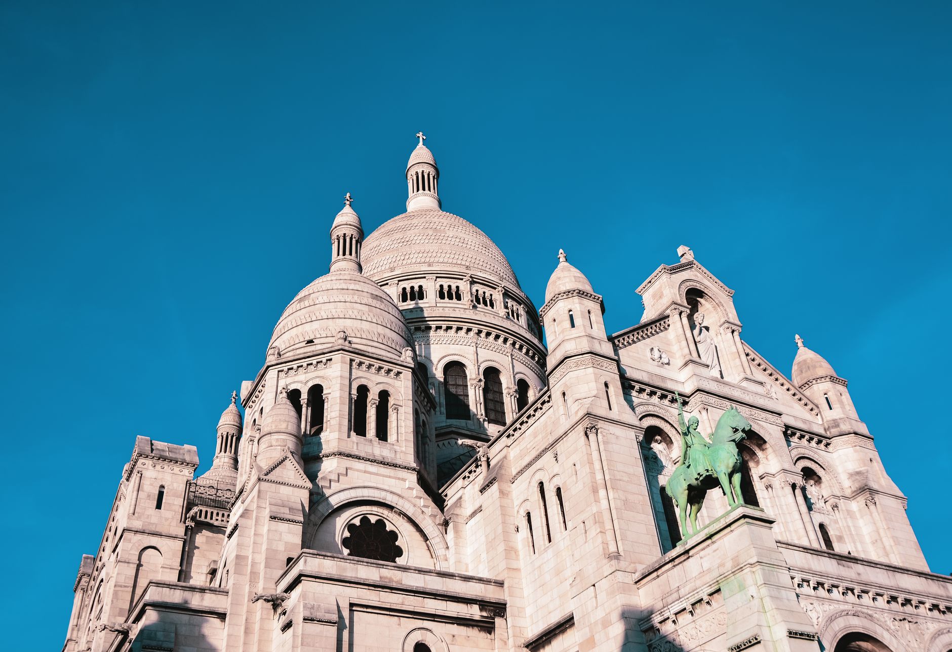 The white domes of the Sacre-Coeur Basilica on Montmartre against a deep blue sky in Paris, France.