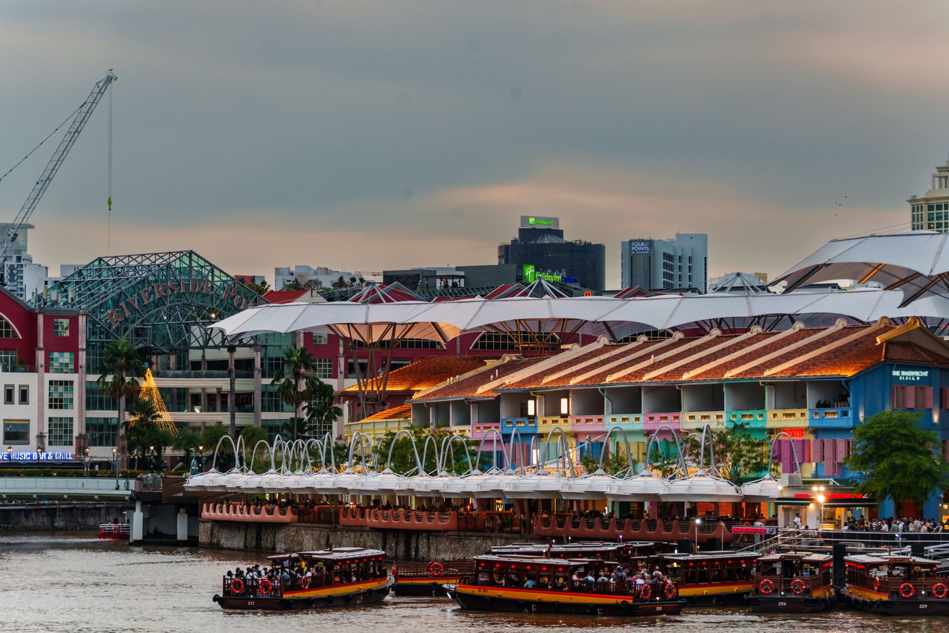 Colourful restored shophouses and bumboats along the Singapore River at Clarke Quay at dusk.